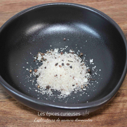 Sel épicé dans un bol noir sur une table en bois, prêt à assaisonner des plats.