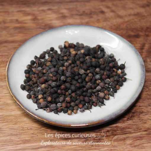 Graines de poivre de Guinée sur une assiette blanche, sur une table en bois. Parfait pour épicer vos plats.