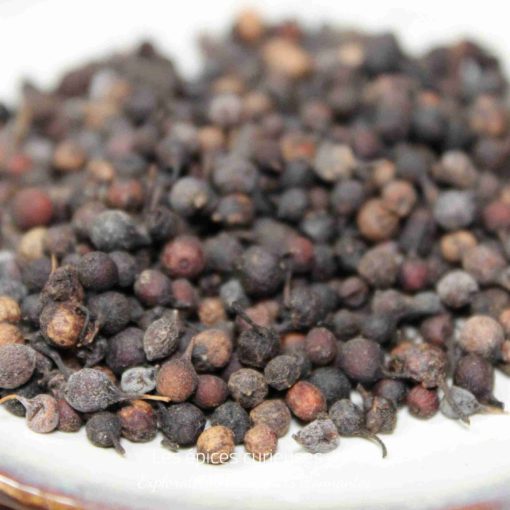 Poivre noir en grains sur une assiette blanche, épice essentielle pour rehausser les saveurs culinaires.