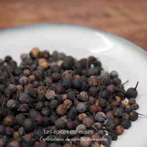 Baies séchées épicées sur assiette blanche, idéal pour assaisonner plats exotiques et créoles.