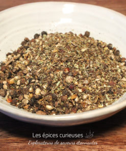 Assortiment de fines herbes et épices séchées dans un bol blanc sur une table en bois.