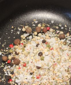 Mélange de poivres et épices variées dans une poêle, idéal pour relever vos plats avec des saveurs intenses.