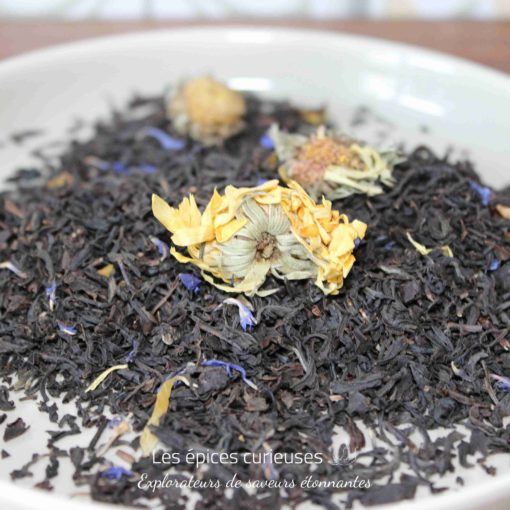 Mélange de thé noir avec des fleurs séchées dans une assiette blanche, prêt pour l'infusion.