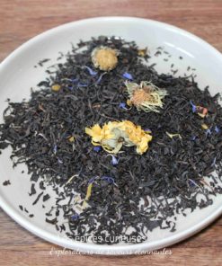 Assortiment de thé noir avec fleurs séchées dans une assiette blanche sur une table en bois.