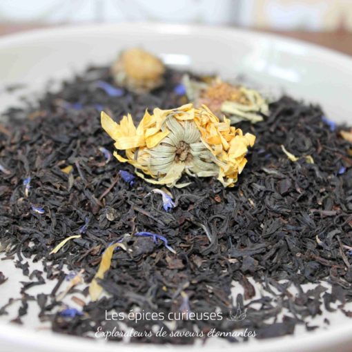 Mélange de thé noir avec fleurs séchées dans une assiette blanche, prêt pour l’infusion.