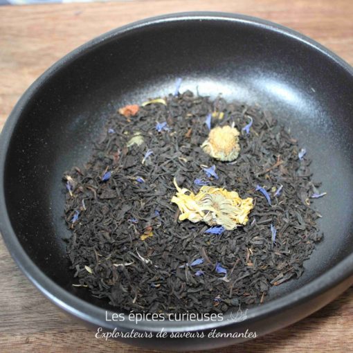 Thé noir en vrac aux fleurs séchées, présenté dans un bol noir sur une table en bois.