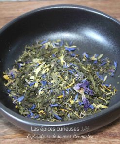 Mélange de thé vert et fleurs séchées dans un bol noir sur table en bois, prêt pour une infusion parfumée et colorée.