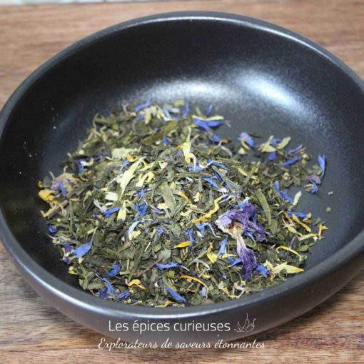 Mélange de thé vert et fleurs séchées dans un bol noir sur table en bois, prêt pour une infusion parfumée et colorée.
