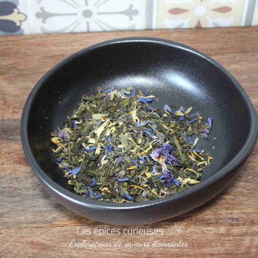 Bol de tisane aux fleurs séchées colorées sur planche en bois, fond carrelé.