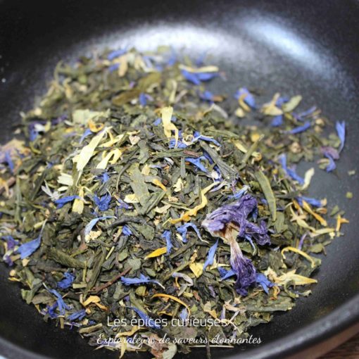 Mélange de thé vert avec fleurs séchées colorées dans un bol noir. Aromatique et visuellement attrayant.