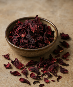 Fleurs d'hibiscus séchées dans un bol en céramique, posées sur une surface en pierre naturelle.