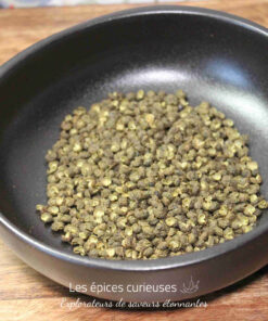 Grains de poivre vert dans un bol noir, posés sur une surface en bois.