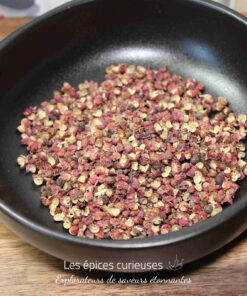 Grains de poivre de Sichuan dans un bol noir sur une table en bois, prêts à être utilisés en cuisine asiatique.