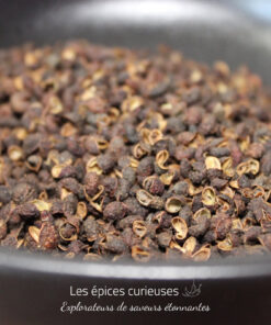 Gros plan sur des grains de poivre de Sichuan dans un récipient noir, offrant une saveur unique et épicée.