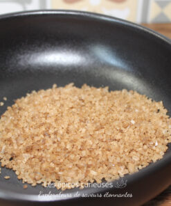 Cristaux de sel brun dans un bol noir sur une table en bois, gros plan sur un condiment naturel et rustique.