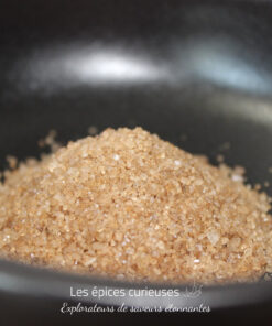 Tas de sucre brun cristallisé dans un bol noir, éclairé délicatement pour en montrer la texture granuleuse.