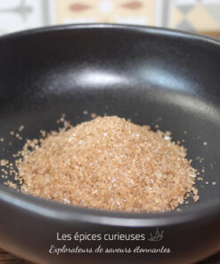 Sucre de canne brun dans un bol noir, idéal pour pâtisserie et boissons. Texture granuleuse et couleur riche.