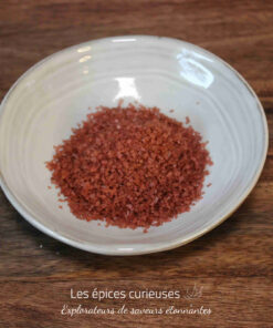 Bol de sel de mer rouge sur une table en bois, idéal pour la cuisine épicée et les plats gourmets.