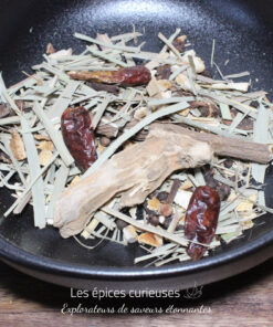 Mélange d'épices et herbes séchées dans un bol noir, idéal pour infusions ou plats aromatiques.