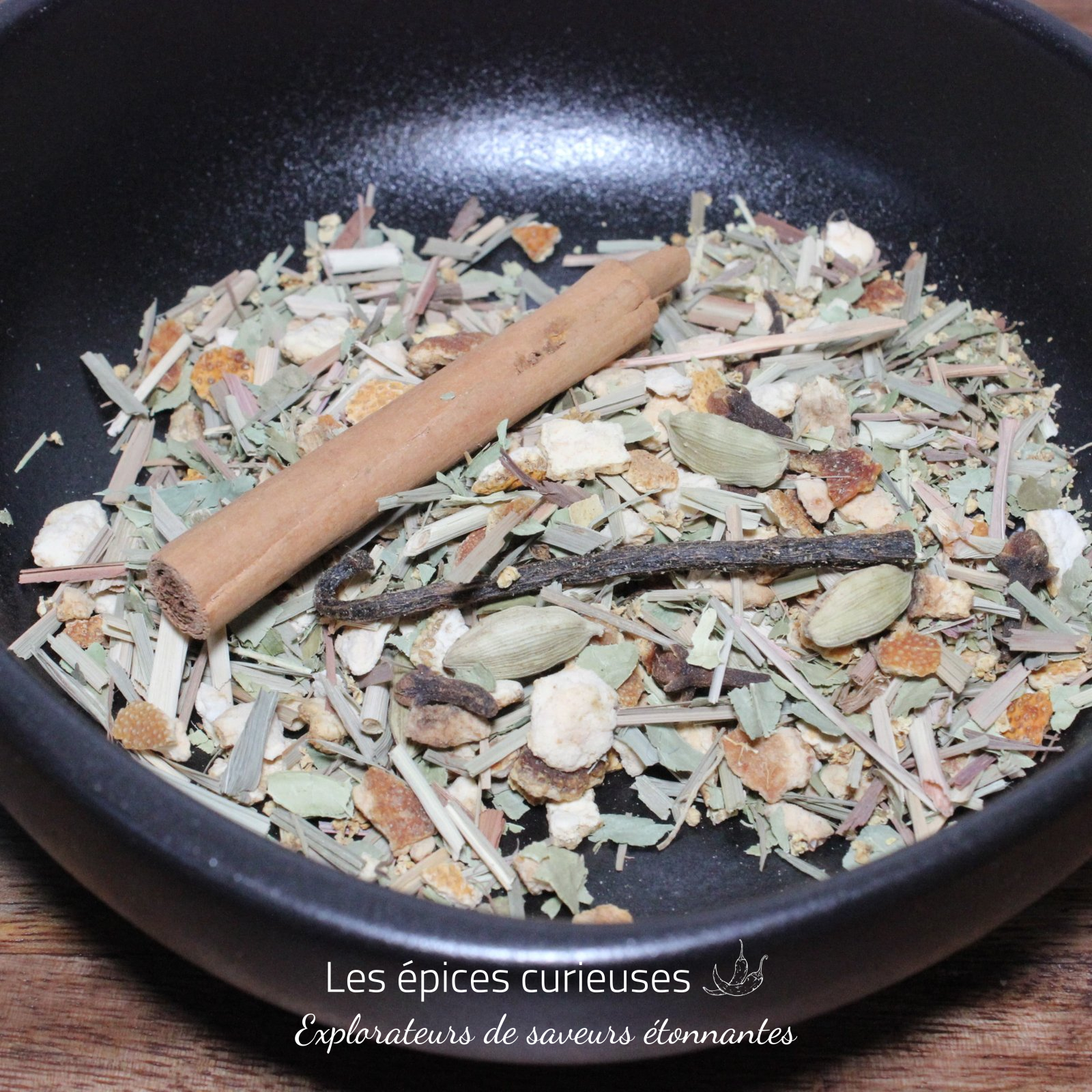 Préparation pour rhum Arrangé Marie Galante – Les épices curieuses Mélange d'épices séchées dans un bol noir, avec bâton de cannelle et cardamome pour infusion parfumée.