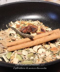 Un mélange d'épices aromatiques dans un bol noir, avec de la cannelle, de l'anis étoilé et des herbes séchées.