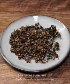 Baies de Sichuan séchées sur une assiette blanche, posée sur une table en bois.