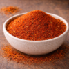 Bol de piment de Cayenne moulu, épice rouge vif sur une table en bois, idéal pour rehausser la saveur des plats.