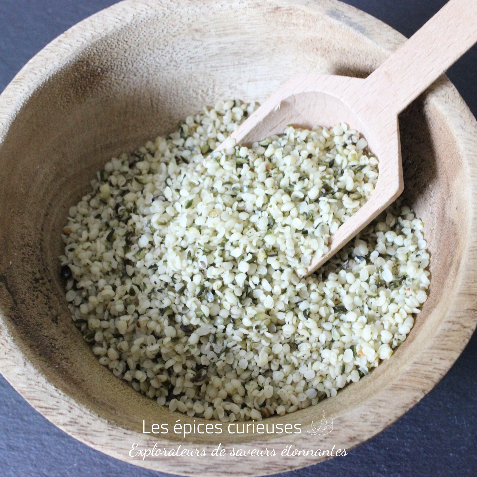 Graines de chanvres décortiquée – Les épices curieuses Graines de chanvre dans un bol en bois avec une cuillère, idéales pour une alimentation saine et riche en protéines.